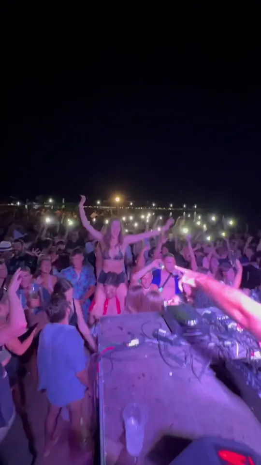 Play clip: the crowd holding up phone lights, seen from behind the decks.